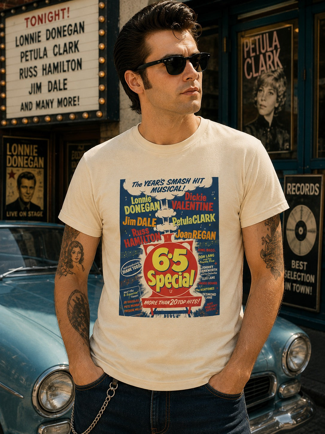 A man wearing a cream-colored graphic t-shirt with a vintage-style musical poster print, standing in front of a blue classic car and a theater storefront. 6-5 special rock and roll show poster.