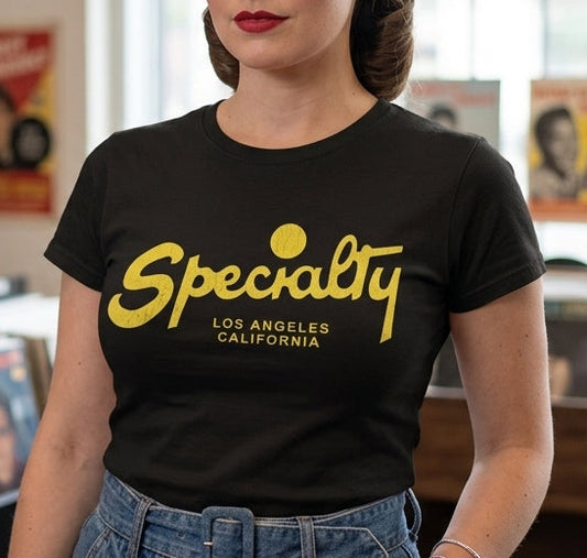 A woman with retro 1950s-style hair stands in a record store wearing a black t-shirt with 'Specialty Los Angeles California' printed in yellow. Vinyl records are visible on shelves in the background.
