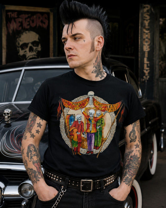 A man with a black mohawk and tattoos wears a black graphic t-shirt featuring the band 'Cult Leader' with skeleton figures. He is posed in front of a vintage car with rock-and-roll themed posters in the background.