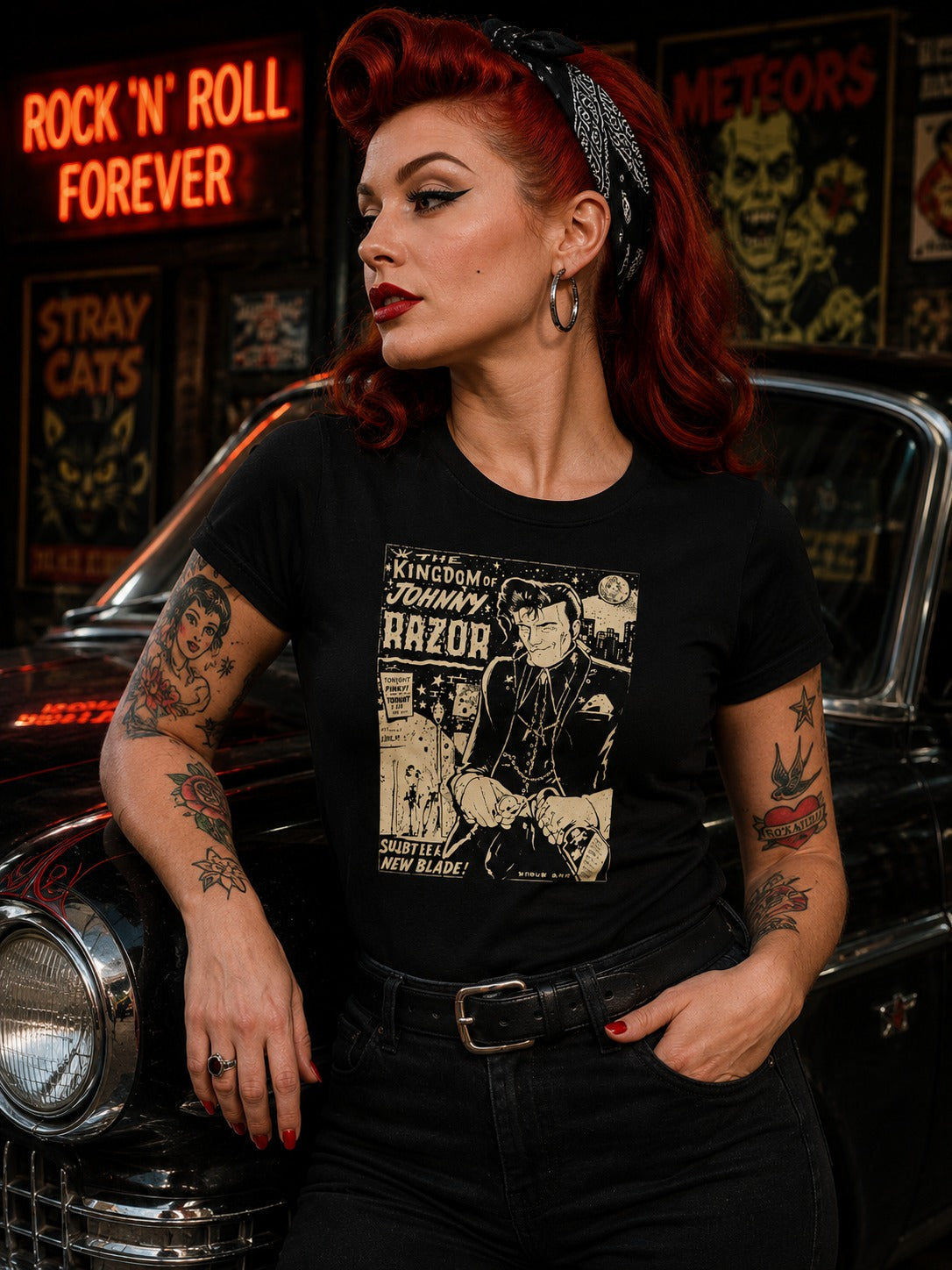 A woman with red hair and tattoos wears a black graphic t-shirt featuring a vintage-style Johnny Depp 'Kingdom of Johnny Razor' print, posed in front of a classic car and a neon sign.